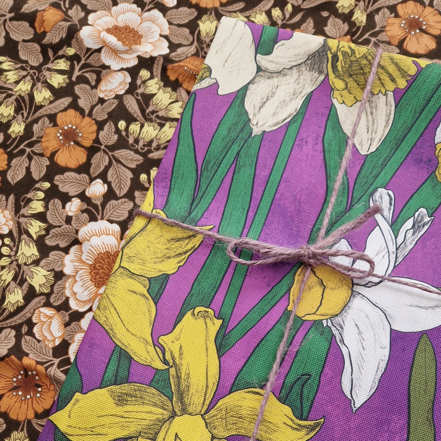 A close up of the top left of the folded hot pink daffodil tea towel. The teatowel is on a dark floral background.