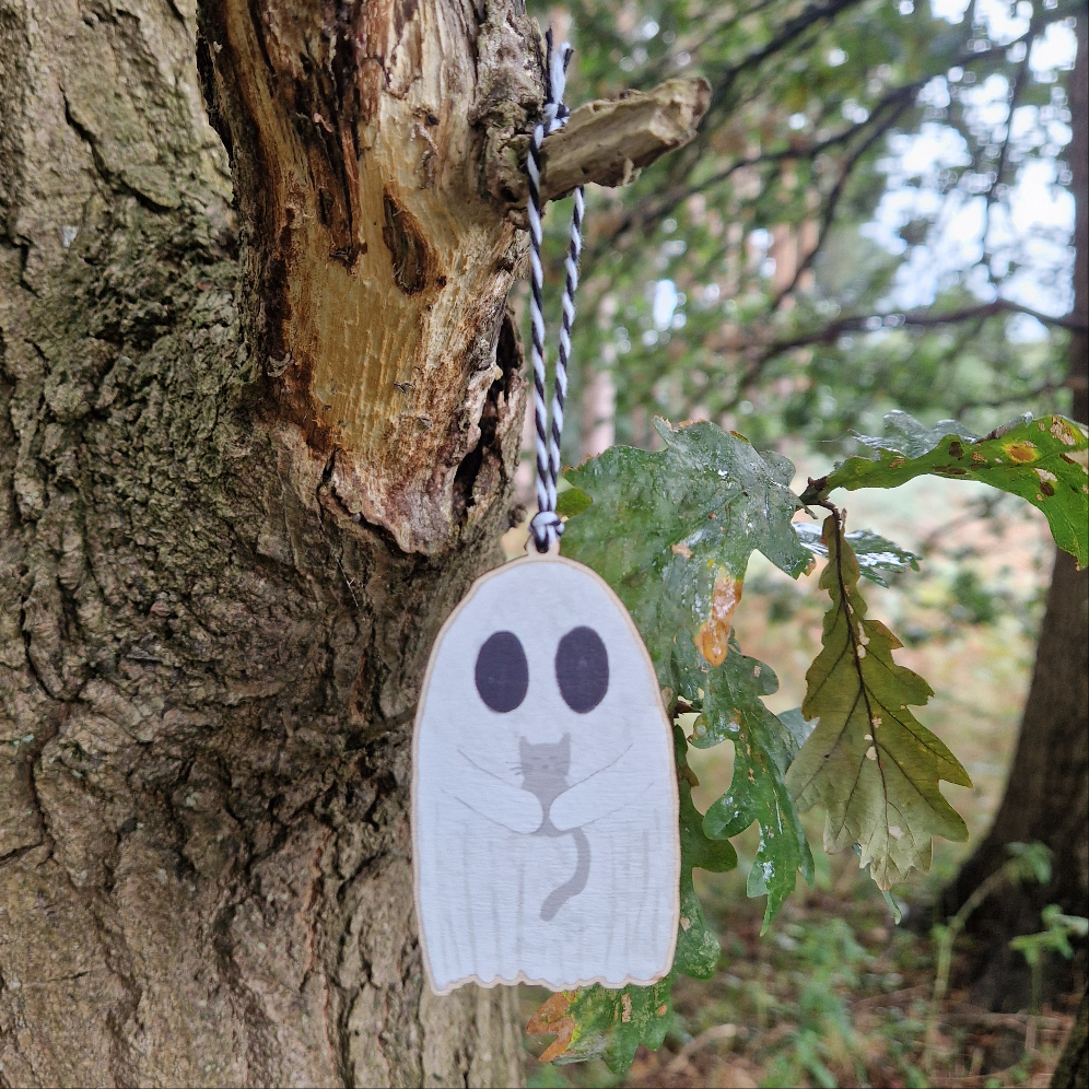 The Ghost With Cat Hanging Wooden Decoration by Duck Egg Designs features a wooden ghost with big black eyes and a painted gray cat, suspended on a string and perfect for adding charming illustrated decor to any outdoor area.