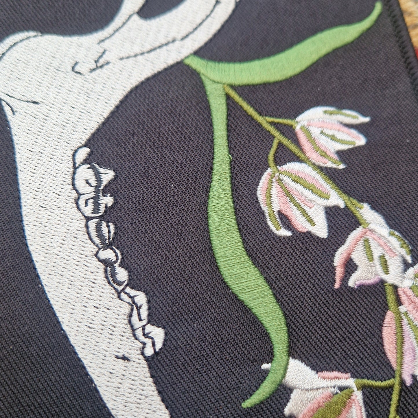 A close up of the black rectangular patch with a deer jawbone and orchids on.
