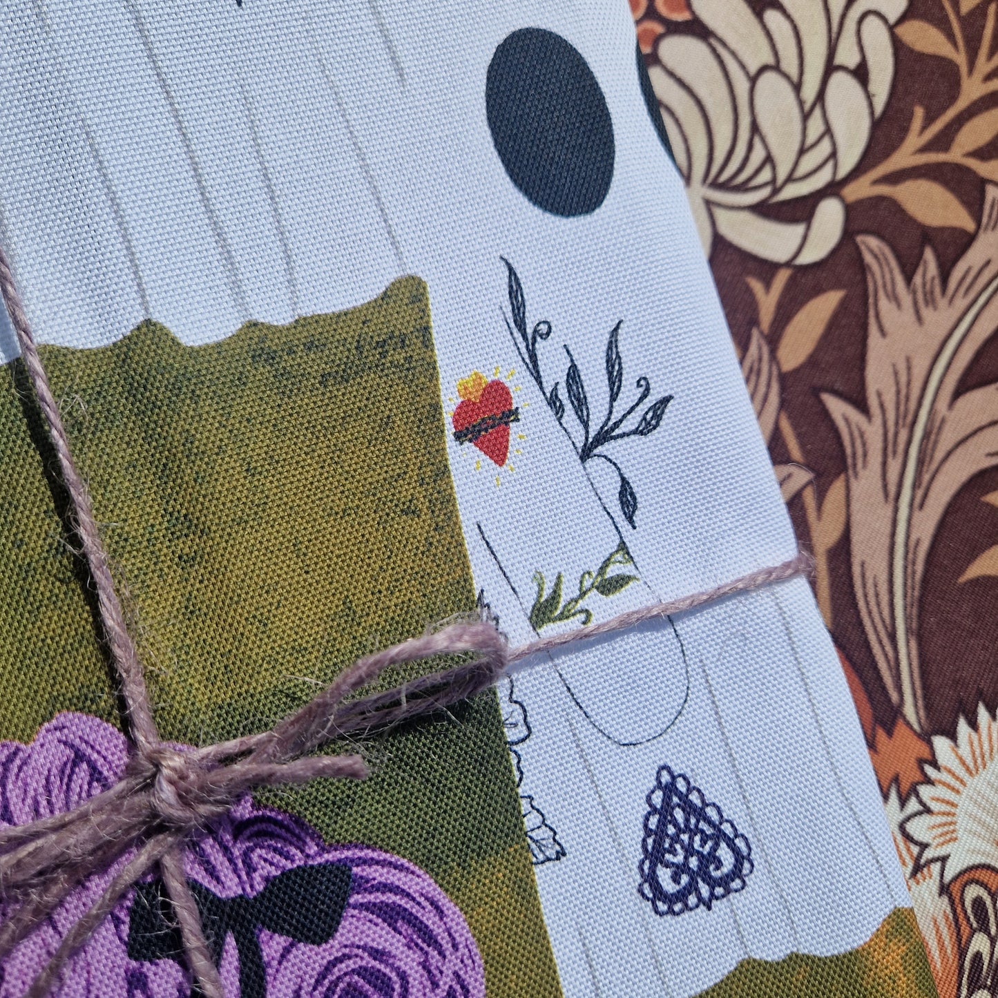 A close-up of Duck Egg Designs A Horde of Ghouls Ghost Tea Towel—100% cotton with colorful abstract ghost patterns—wrapped around a package tied with twine, set against a brown floral-patterned background.