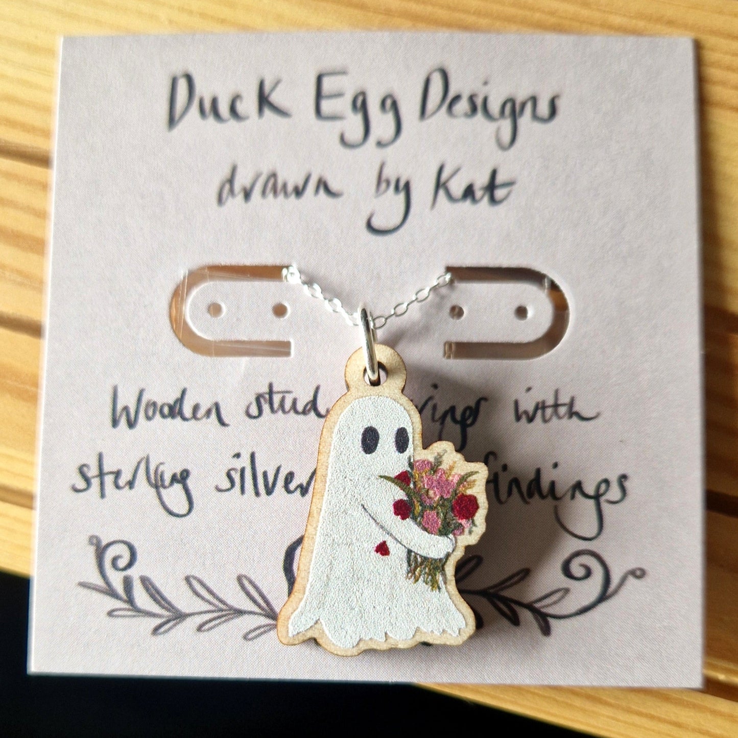 Ghost-shaped pendant with floral design on a card with 'Duck Egg Designs' text
