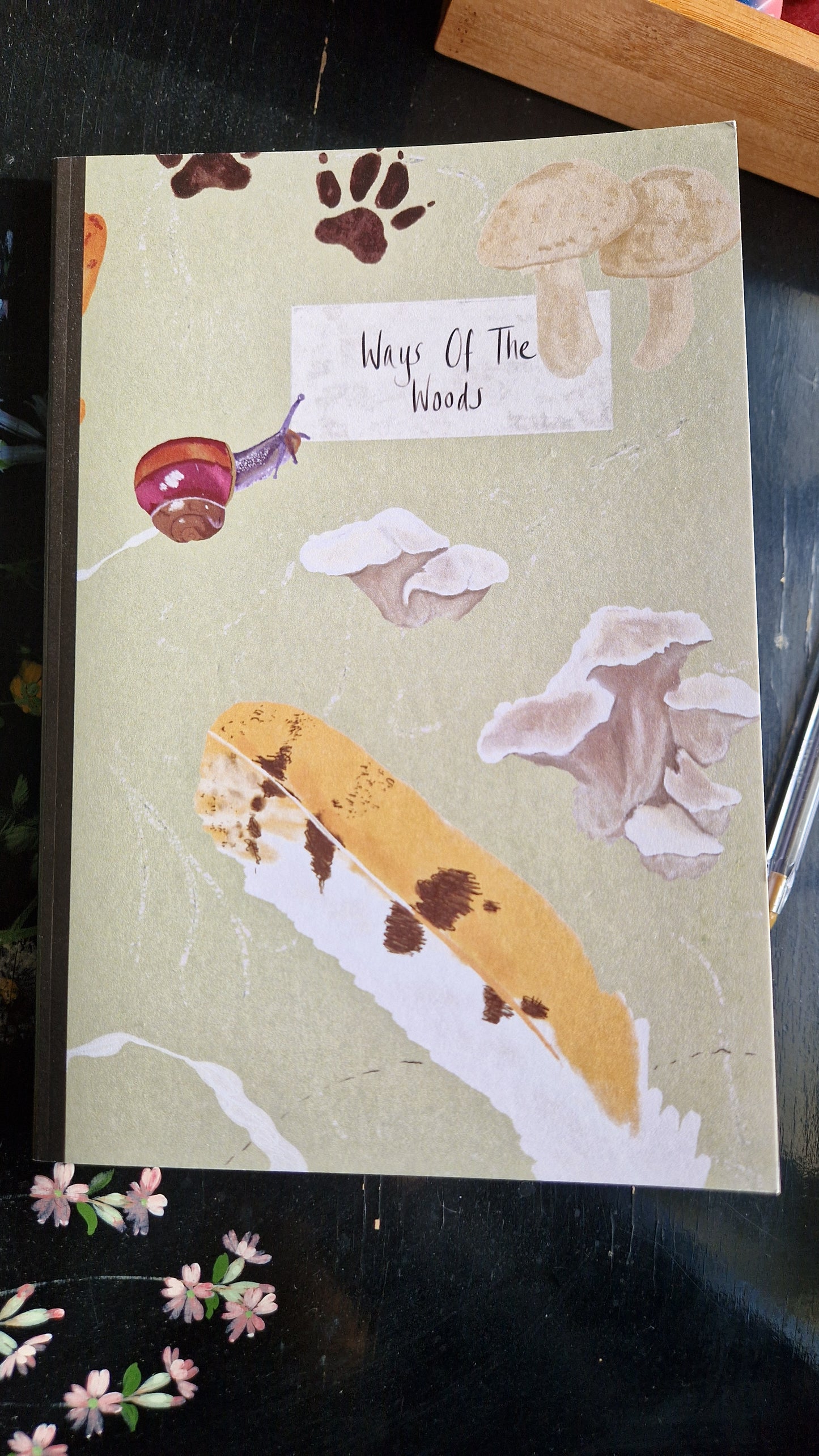 The Reckless Attack Notebook by Duck Egg Designs is crafted with recycled paper and features a cover illustrated with a snail, feather, fungi, animal paw prints, and wildflowers—perfect for campaign notes.