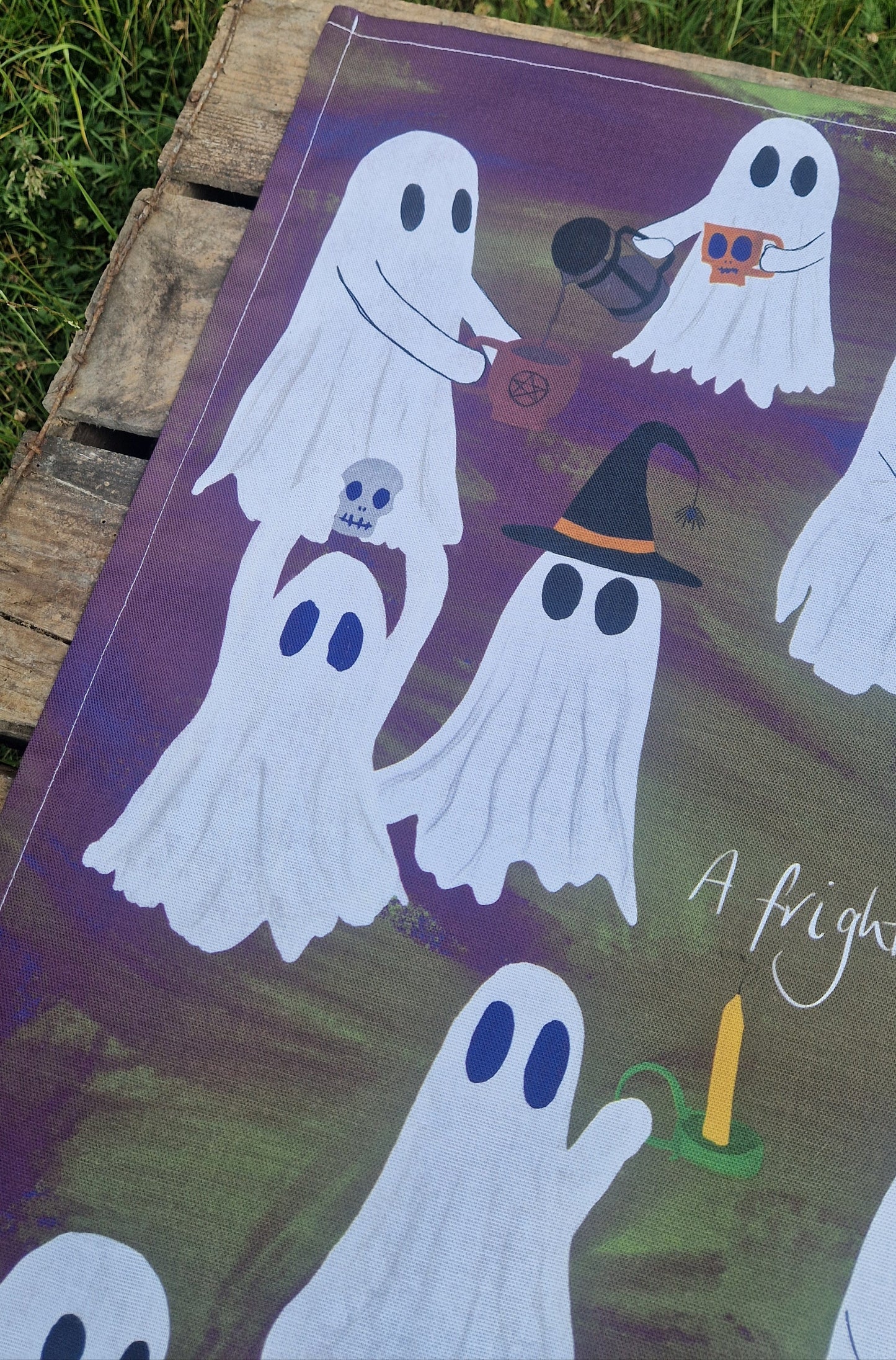 Ghost-themed tea towel on a wooden surface with grass in the background