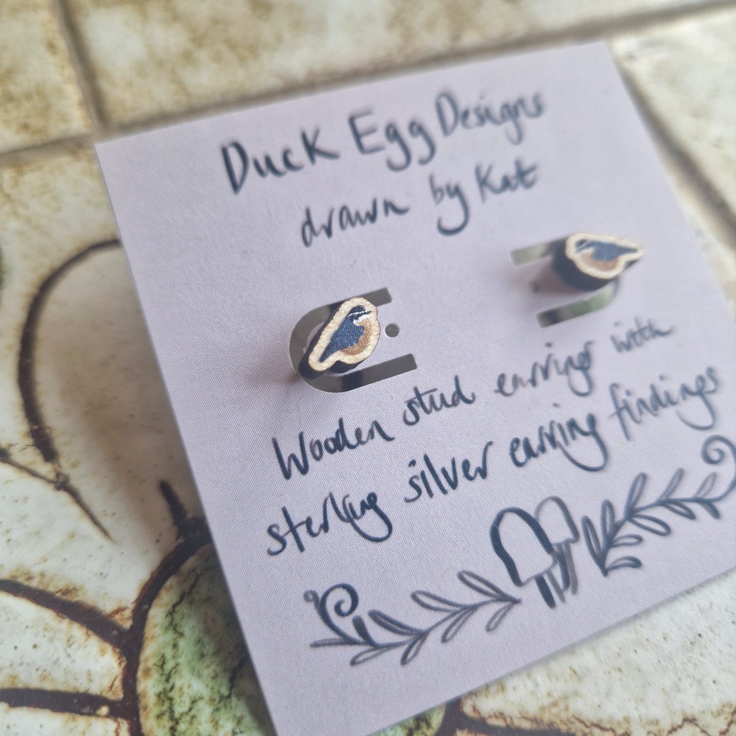 Nuthatch Bird Wooden Stud Earrings by Duck Egg Designs are crafted from FSC certified wood with sterling silver findings, featuring charming doodles and presented on a card reading "Duck Egg Designs drawn by Kat.
