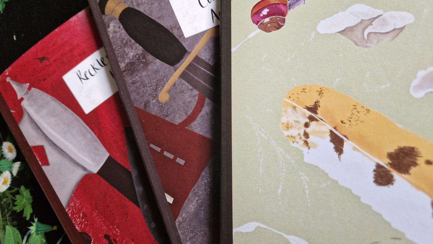 Three notebooks on top of each other in a fan shape - red, grey and green notebooks with different designs.