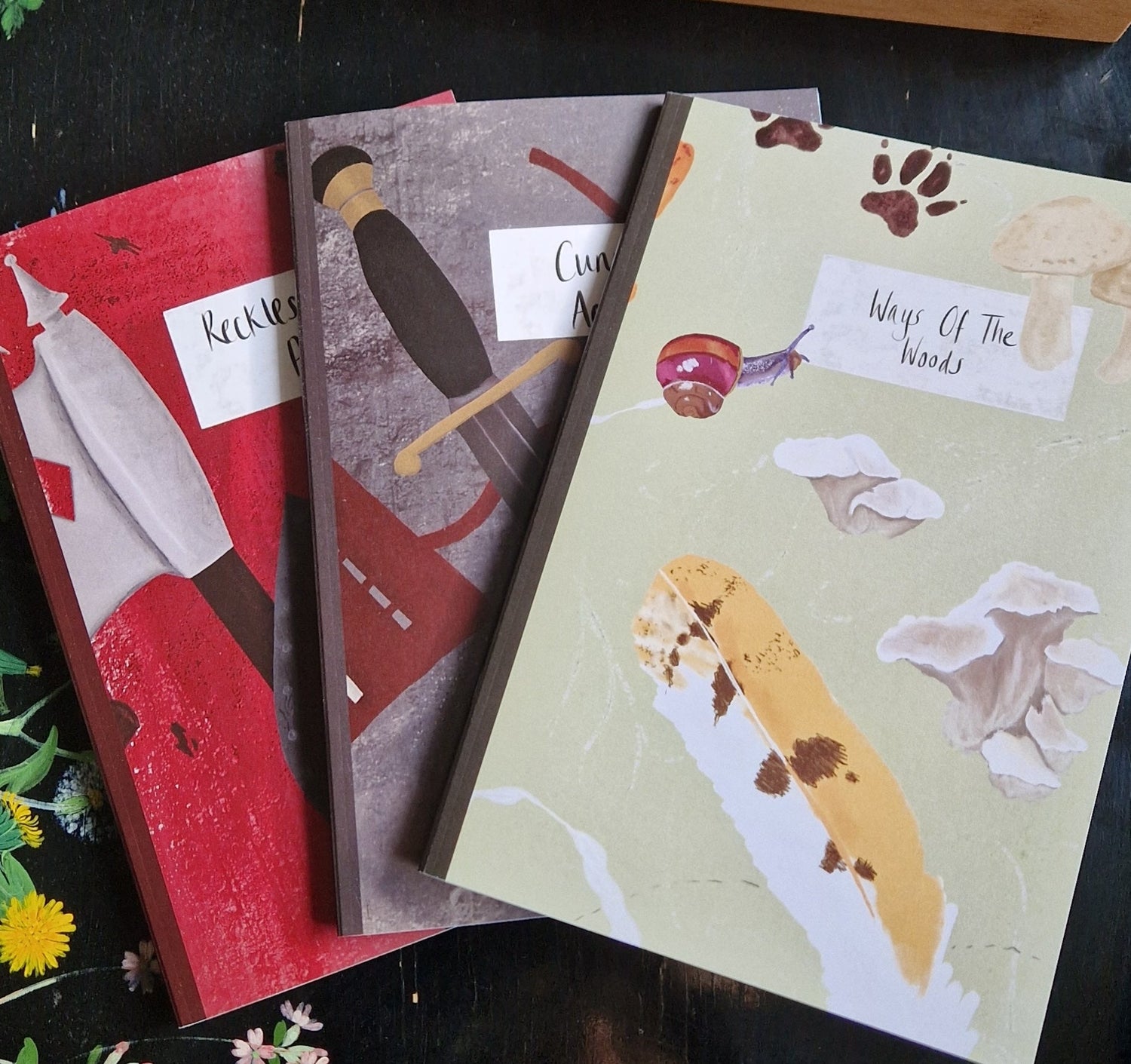 Three colourful notebooks of red, grey and green featuring dungeons and dragons inspired designs sit on a black table.