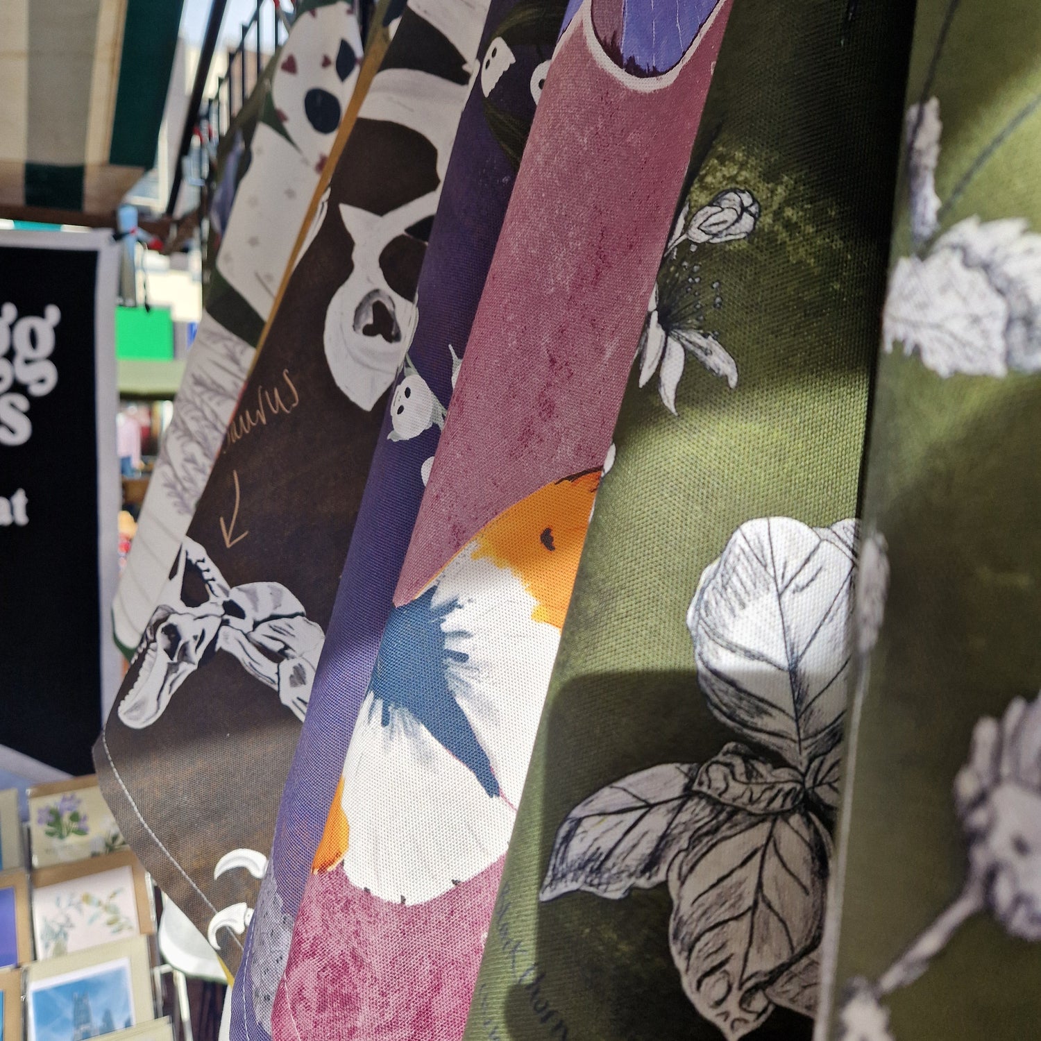 A close up of some colourful hanging tea towels with a card stand and pennant hanging in the background.