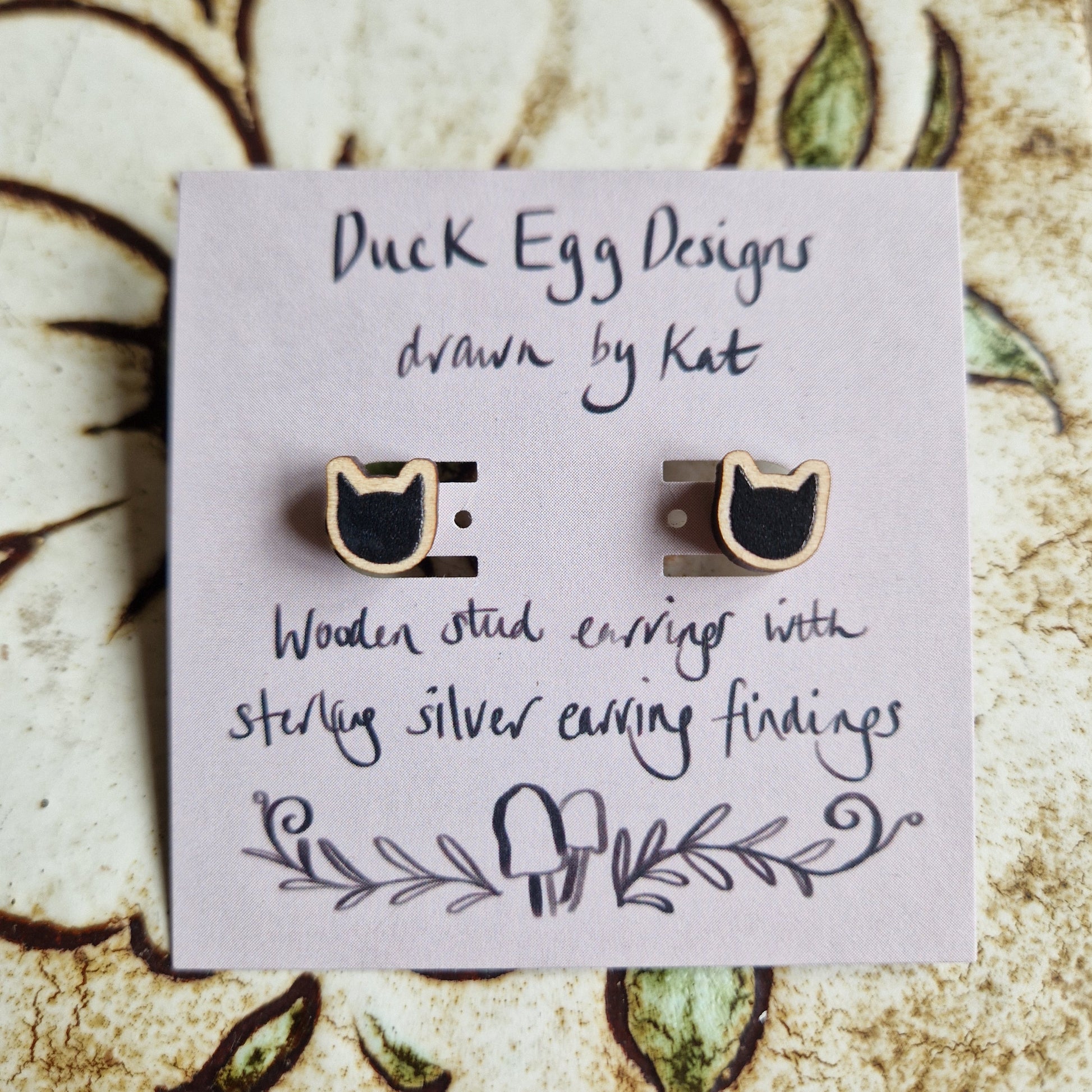 Black Cat Stud Earrings by Duck Egg Designs are crafted from wood with sterling silver backs, and come displayed on a charming hand-drawn card.