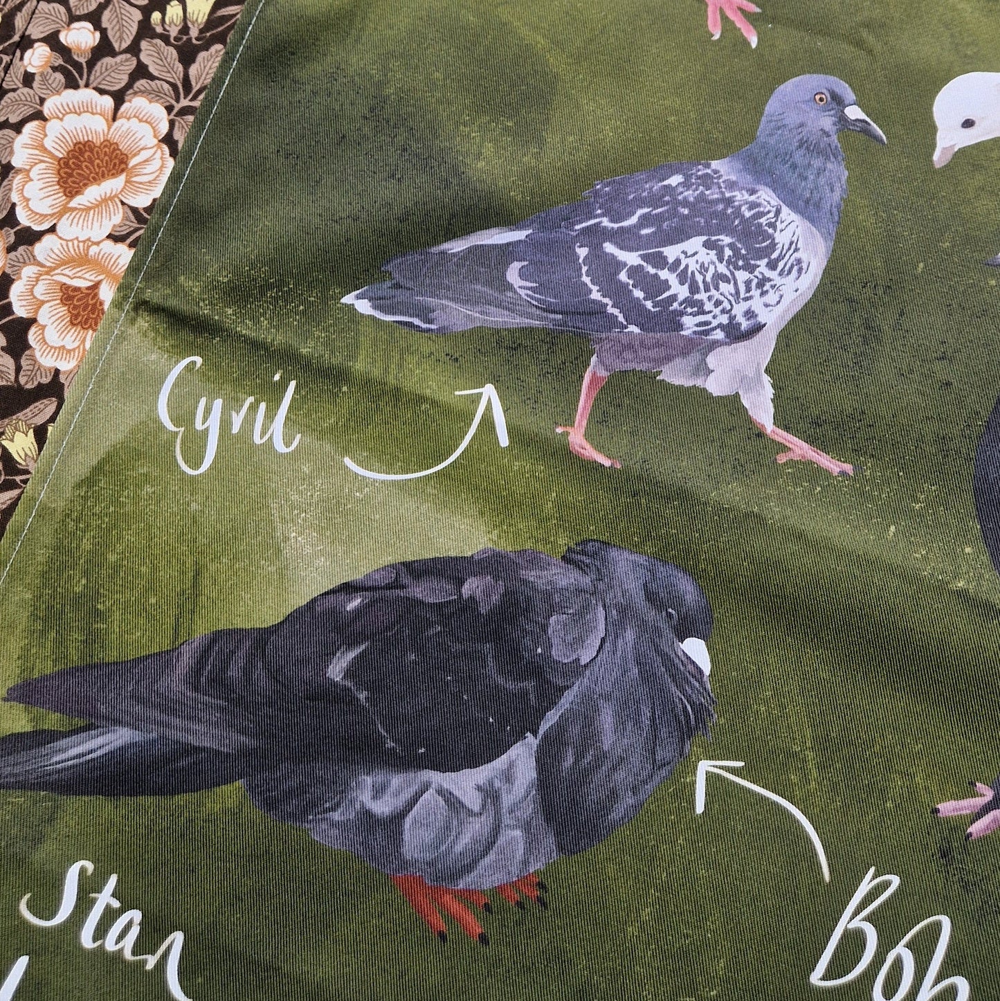A close up of the green teatowel showing three of the different pigeons and their names. To the left of the teatowel you can see a retro floral patterned fabric.