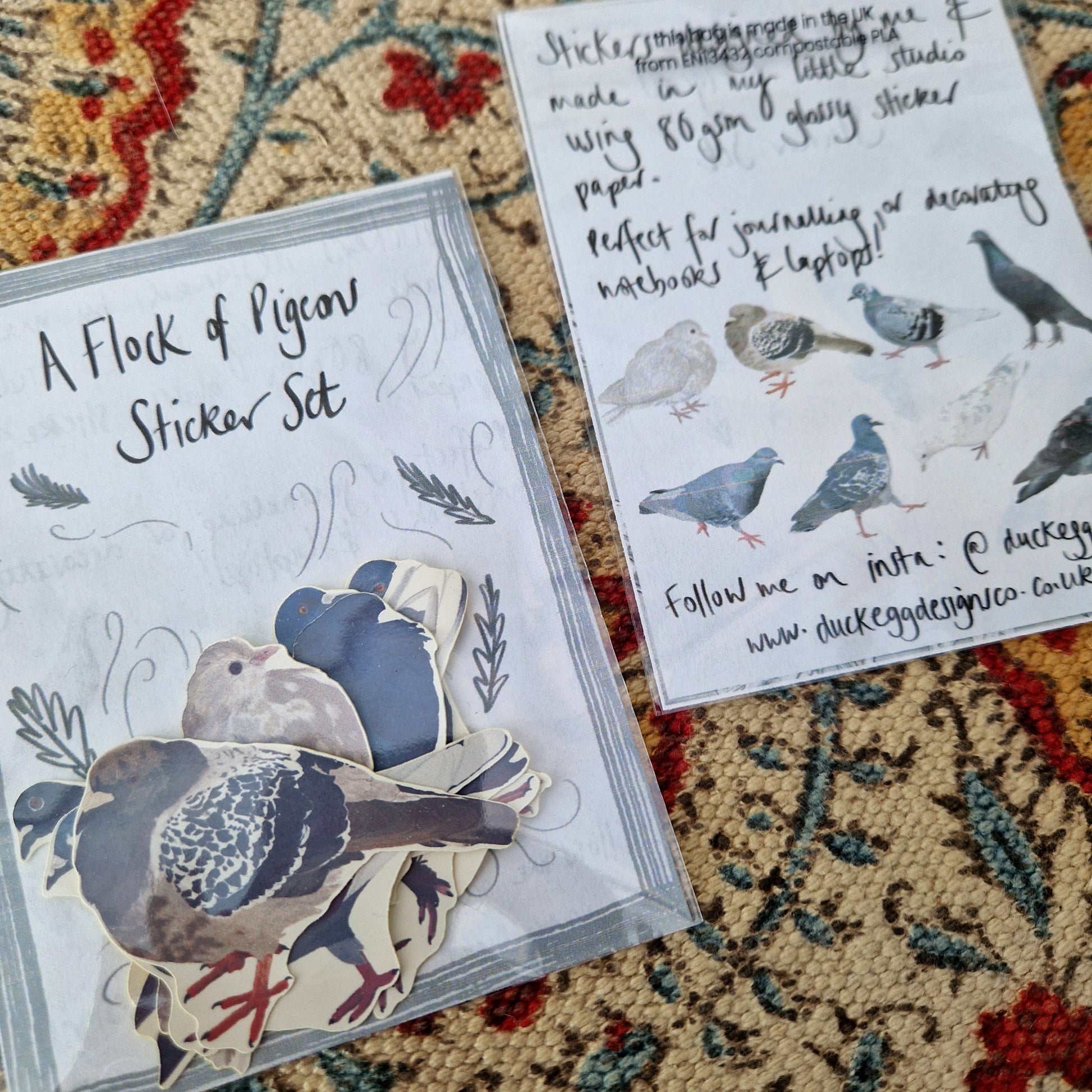 Two sticker sets next to each other - one with the top of the sticker set facing upward showing the stickers inside and one face down showing the sticker set information and the illustrations of all the stickers inside. They're both sat on a patterned fabric background.