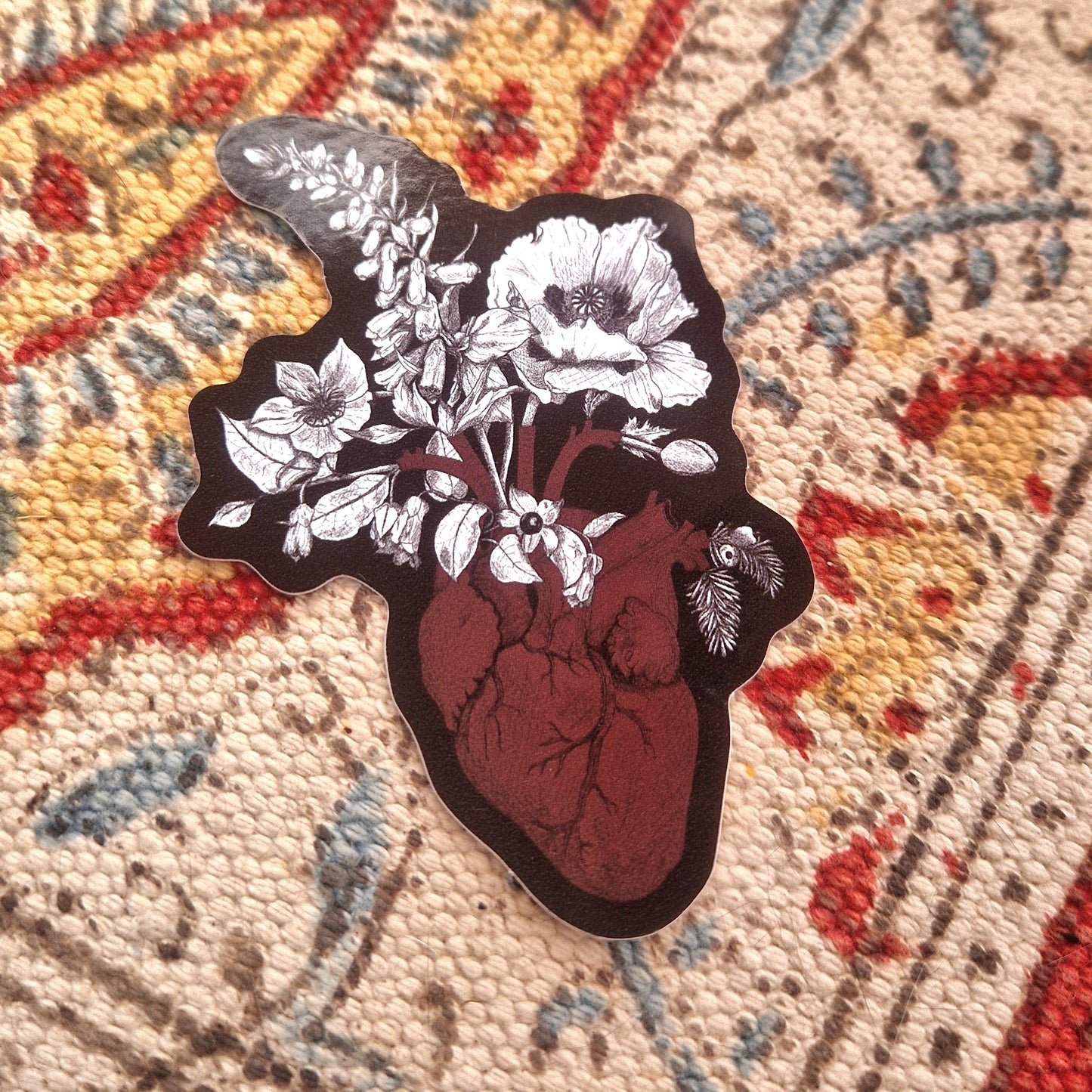 A heart shaped vinyl sticker with poisonous plants growing from the heart, sits on a fabric background.