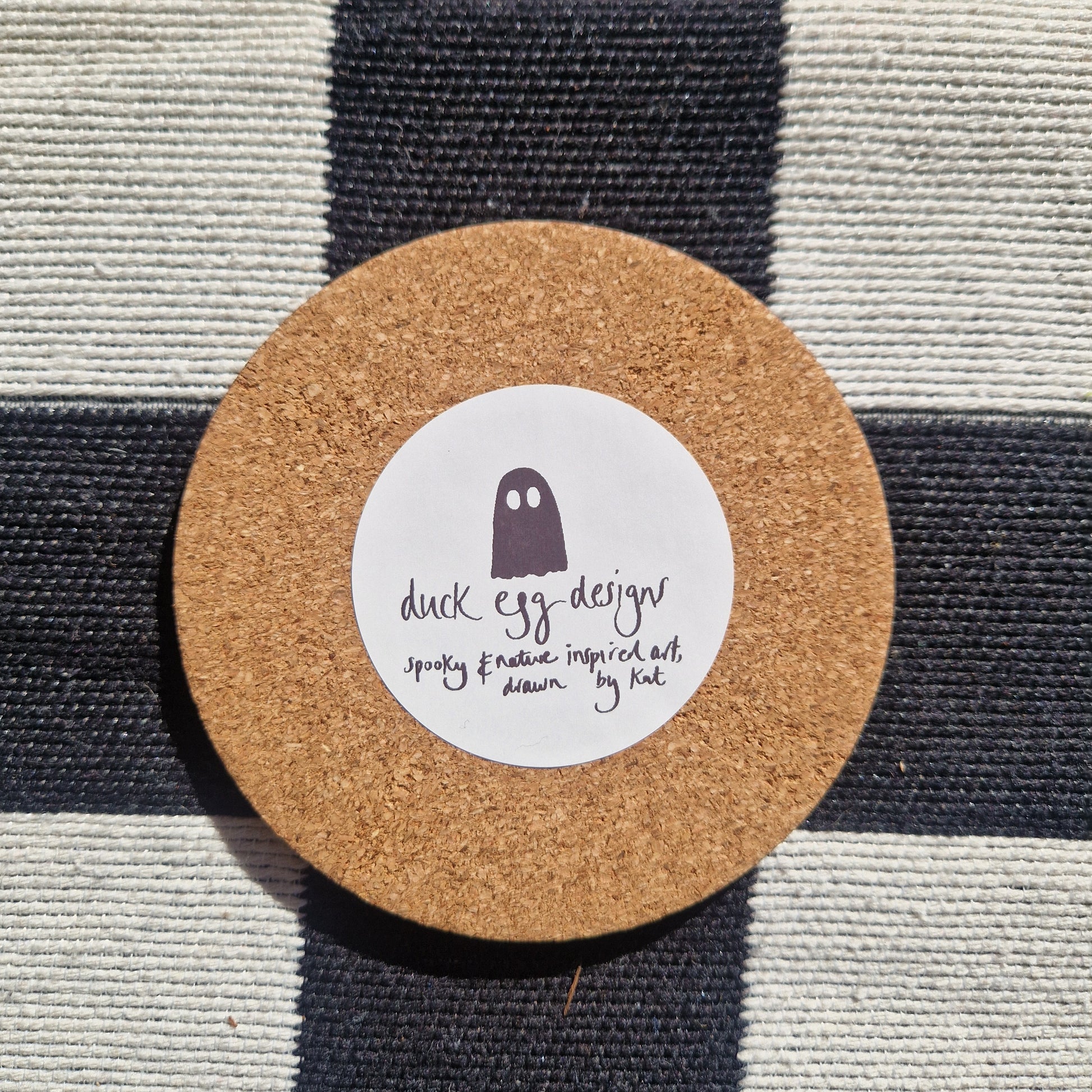 The base of the round coaster showing the cork bottom featuring a white round sticker with the black ghost duck egg designs logo.