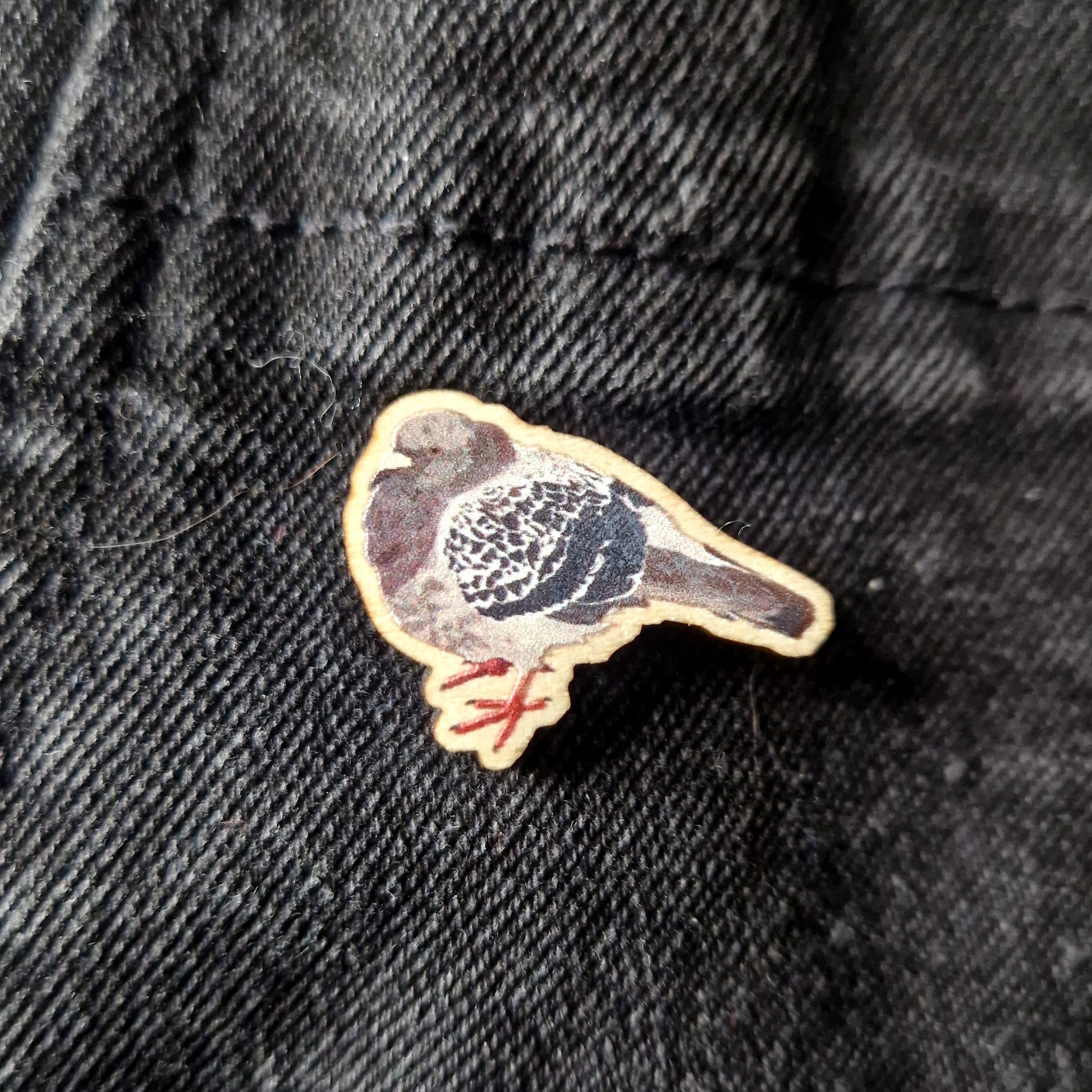 A round wooden pigeon pin sits on a black denim fabric.