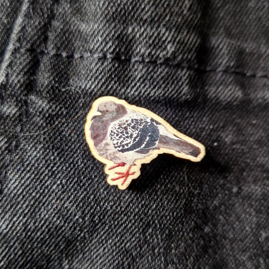 A round wooden pigeon pin sits on a black denim fabric.