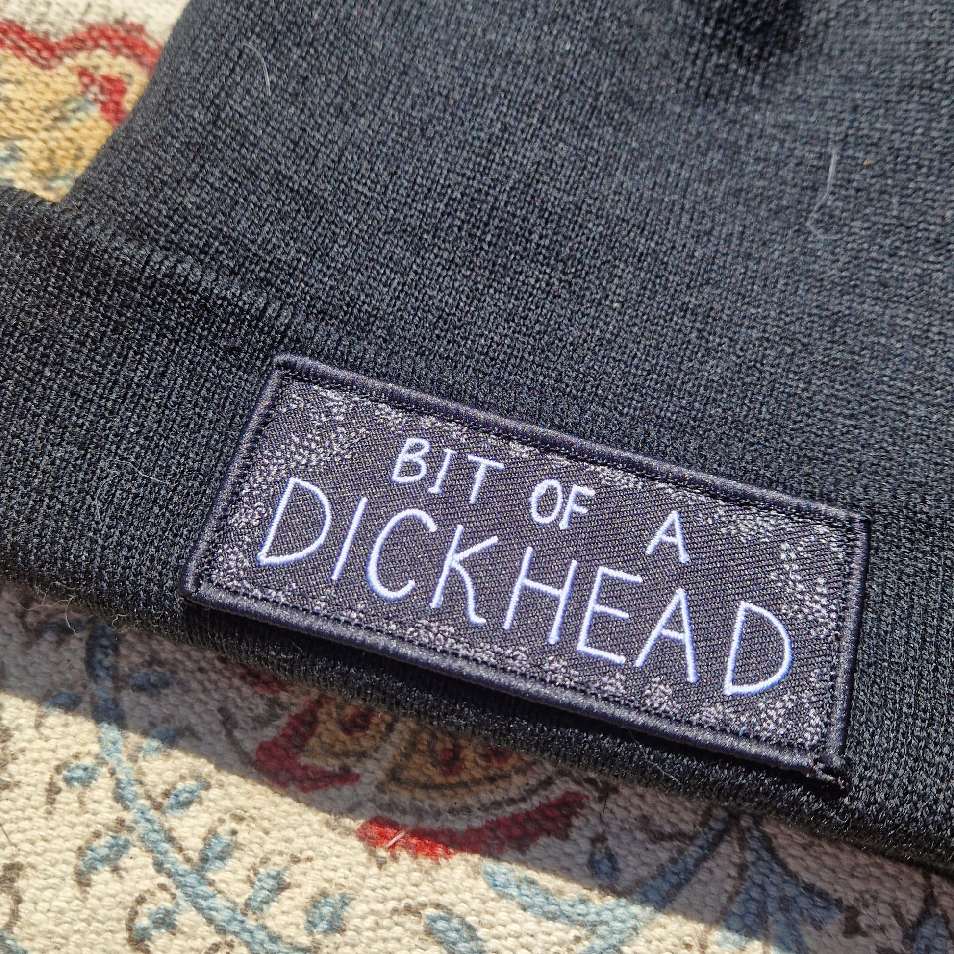 A close up view of the black beanie showing the trailing leaf pattern around the edge of the patch.