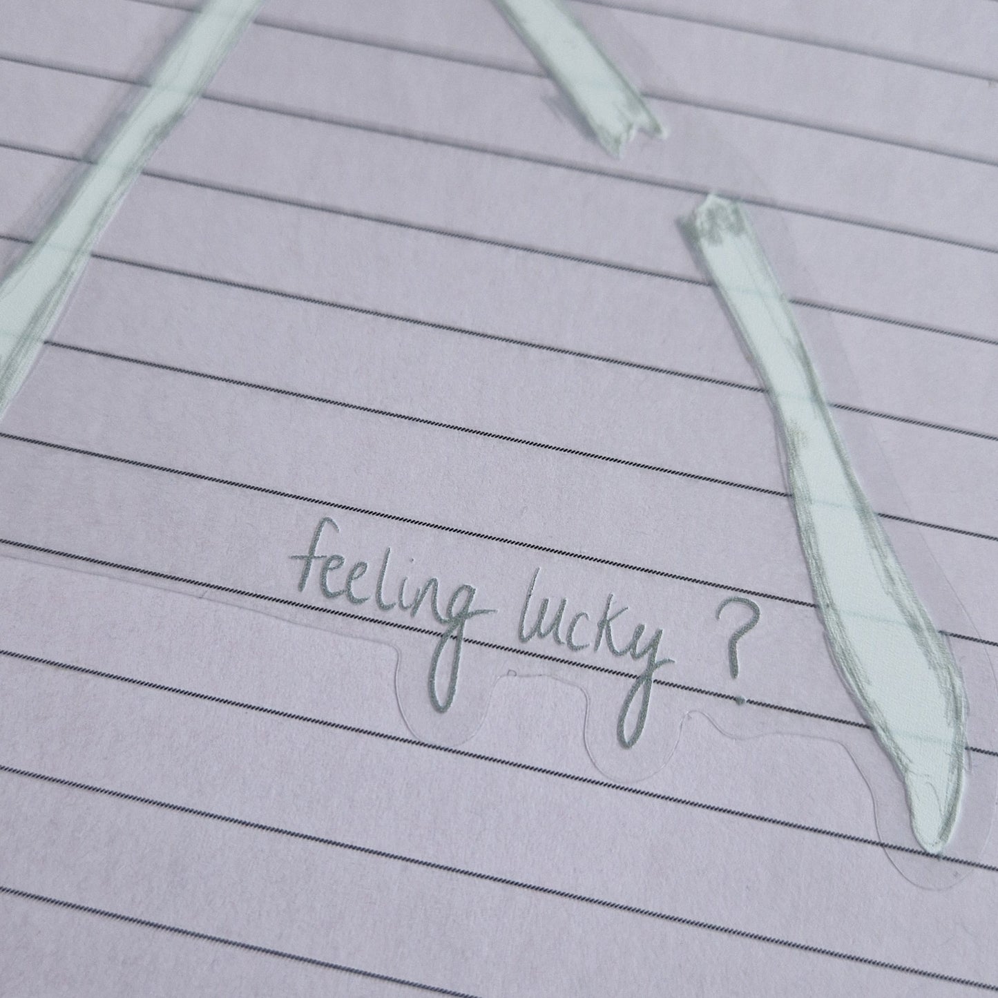 A close up of the bottom left of the sticker showing the grey handwriting that reads 'feeling lucky?' the broken wishbone section is visible above it and the sticker has a transparent background.
