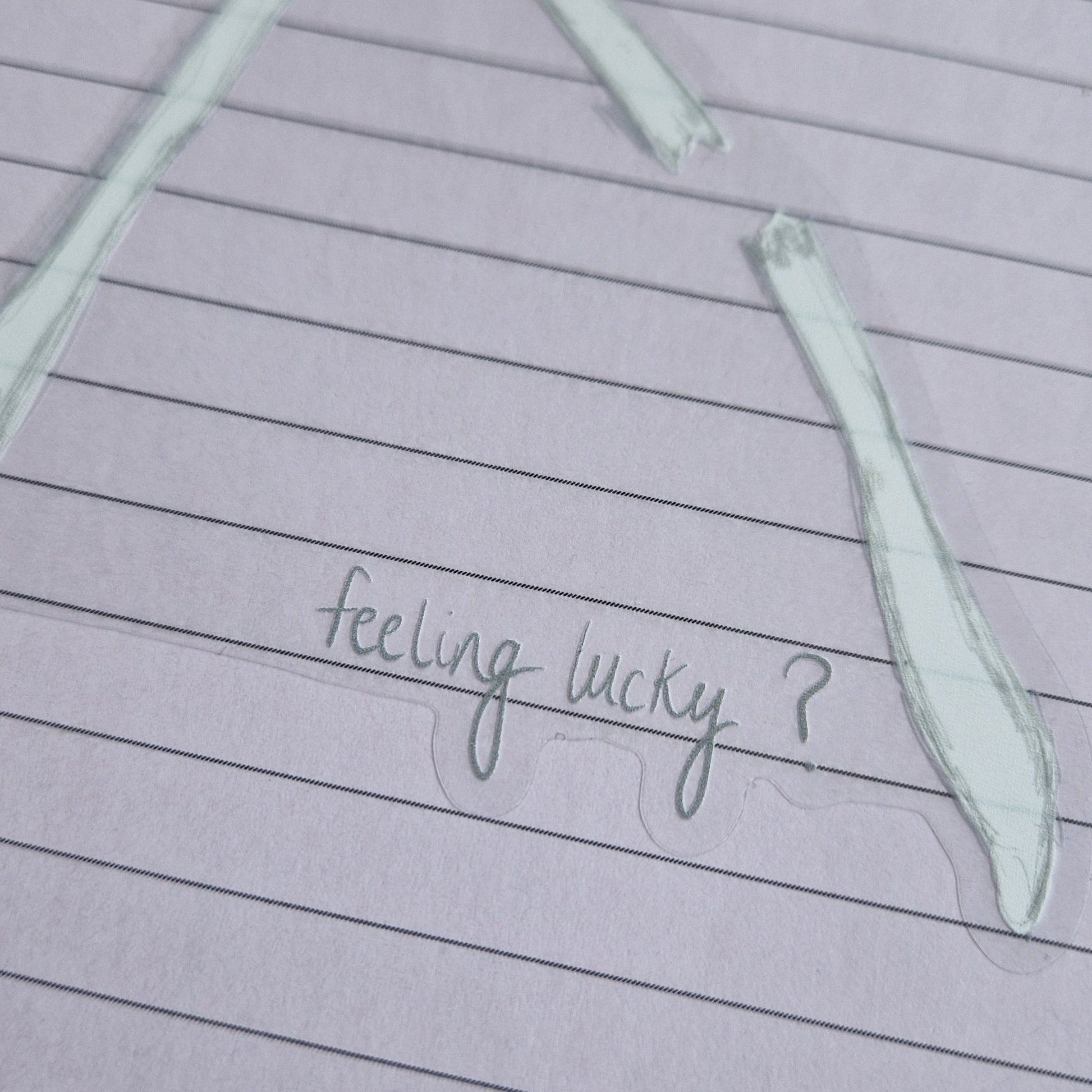 A close up of the bottom left of the sticker showing the grey handwriting that reads 'feeling lucky?' the broken wishbone section is visible above it and the sticker has a transparent background.