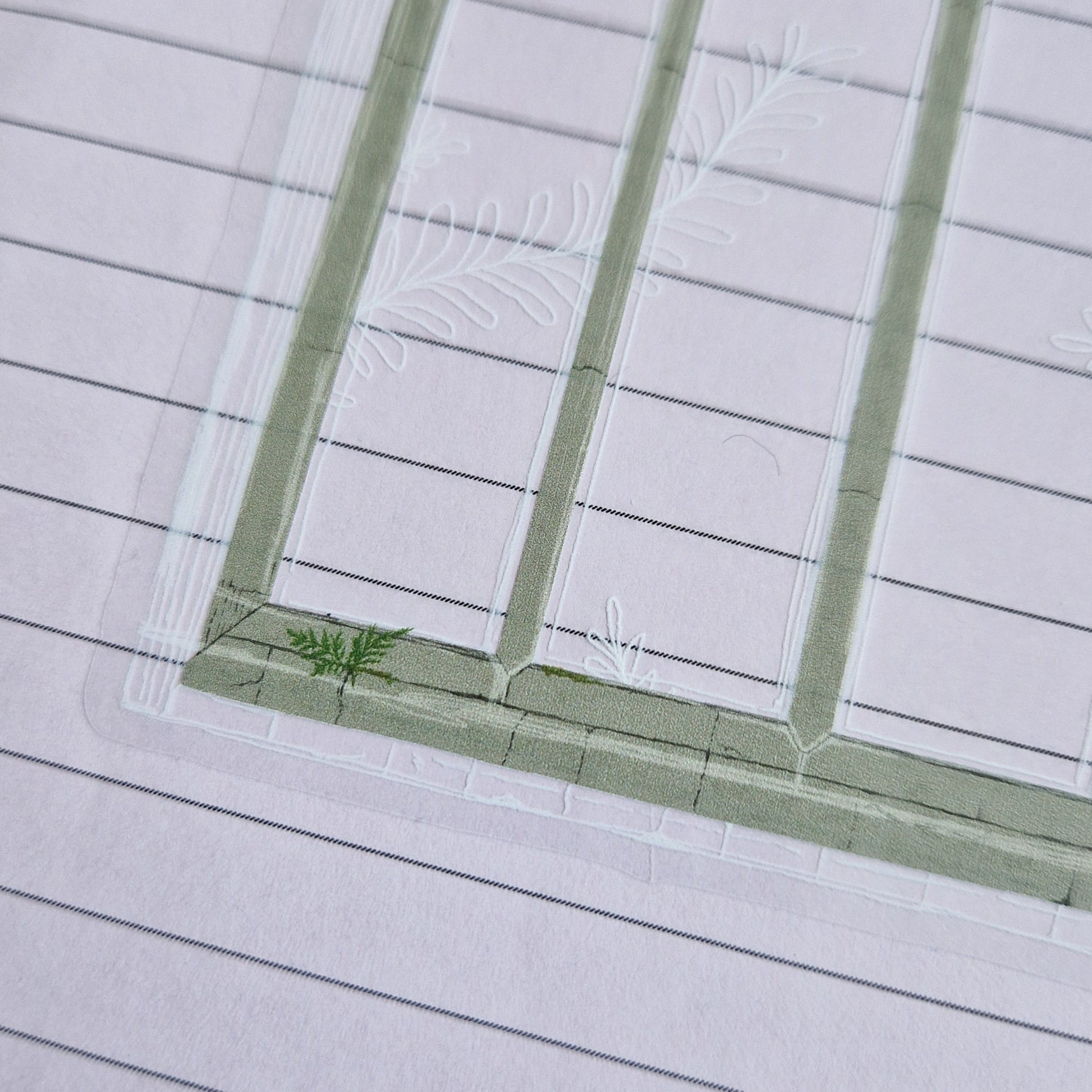 A close up of the bottom left of the cathedral window sticker which has a transparent background. Showing the frame of the window as well as a little fern plant growing out of it and white line drawing showing the edge of the window framing and ferny fronds growing across the window.