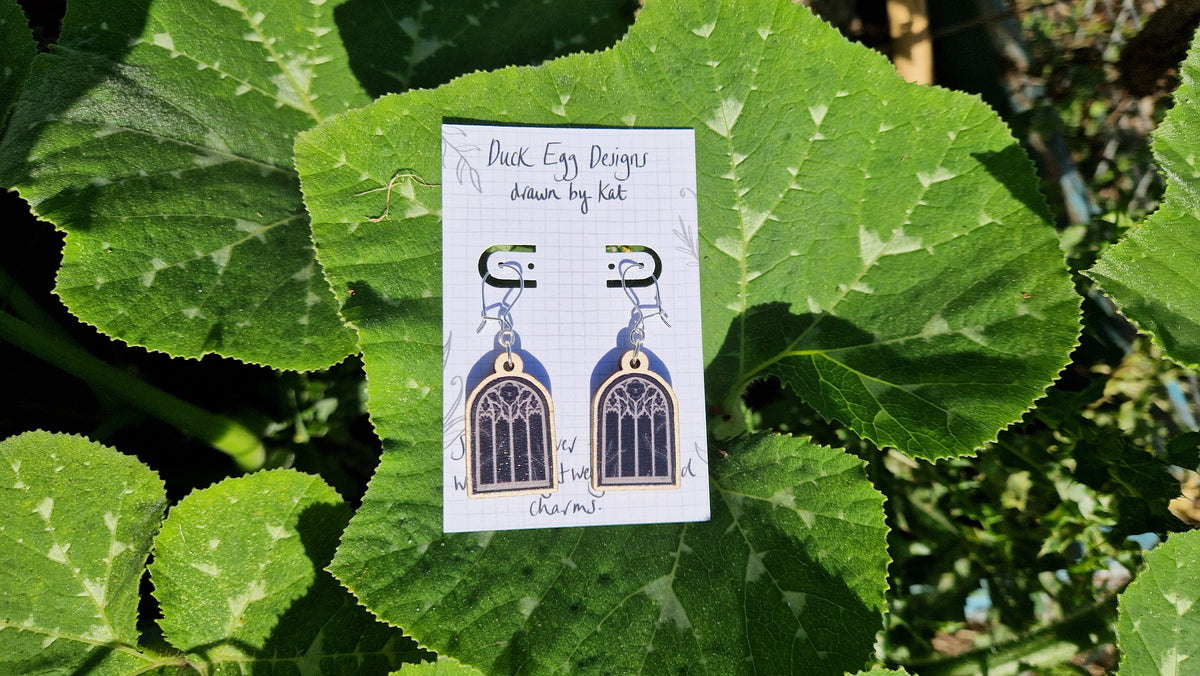 A pair of cathedral window earrings sit on a white backing card on a large green leaf.