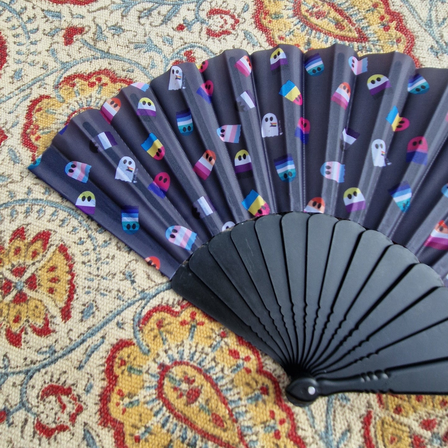 A close up of the black fan covered in pride flag ghosts. The fan rests on a patterned rug.