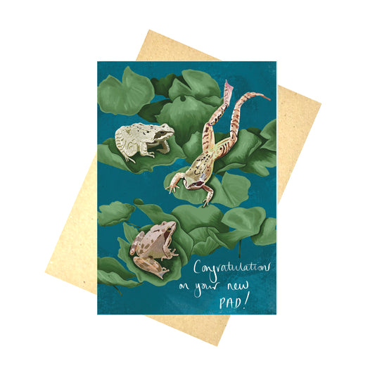A rich blue greetings card featuring green lily pads with three frogs on and the words 'Congratulations on your new pad!' in white handwriting.