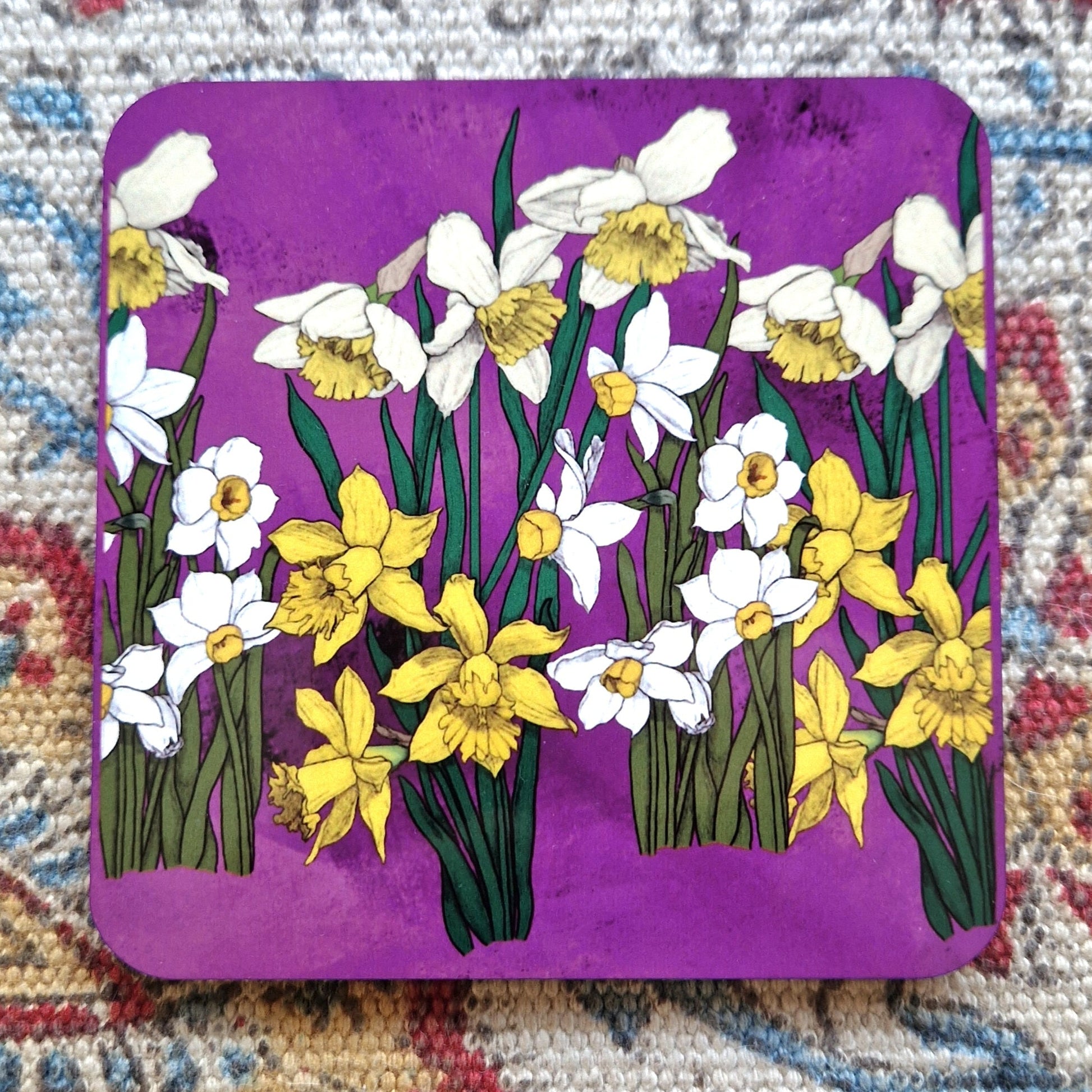 A bright magenta square coaster featuring a repeating daffodil design with rich and pale yellow/white flowers.