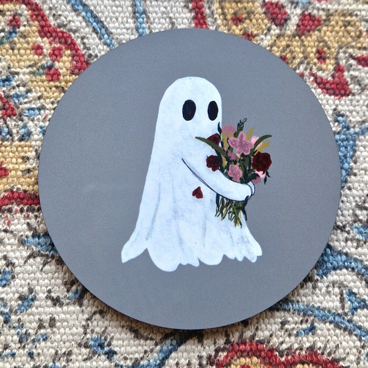 A round grey coaster with a ghost holding a bunch of flowers.