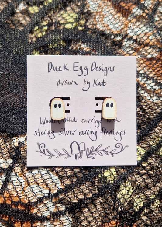 A pair of white ghost studs sit on a light purple backing card that has the words 'Duck Egg Designs drawn by Kat' in black writing. Behind the backing card is a black lace fabric over a floral fabric.