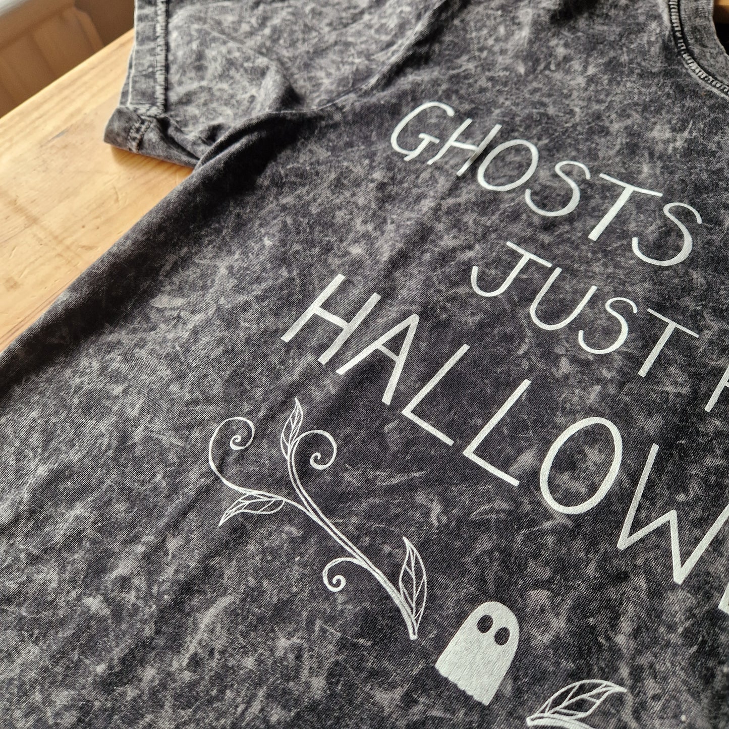A close up of the mottled grey tshirt showing the acid wash of the fabric. A close up view of the handwritten text as well as the ghost and leafy tendril design.