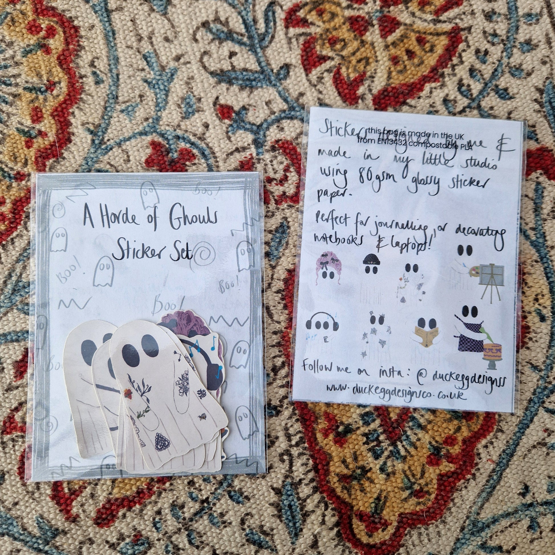 Two sticker sets sit next to each other on a patterned fabric background. One is facing up showing the ghost stickers inside and the words 'Horde of Ghouls Sticker Set' across the top in black handwriting. One is facing down showing the sticker set information and the eight different sticker designs.