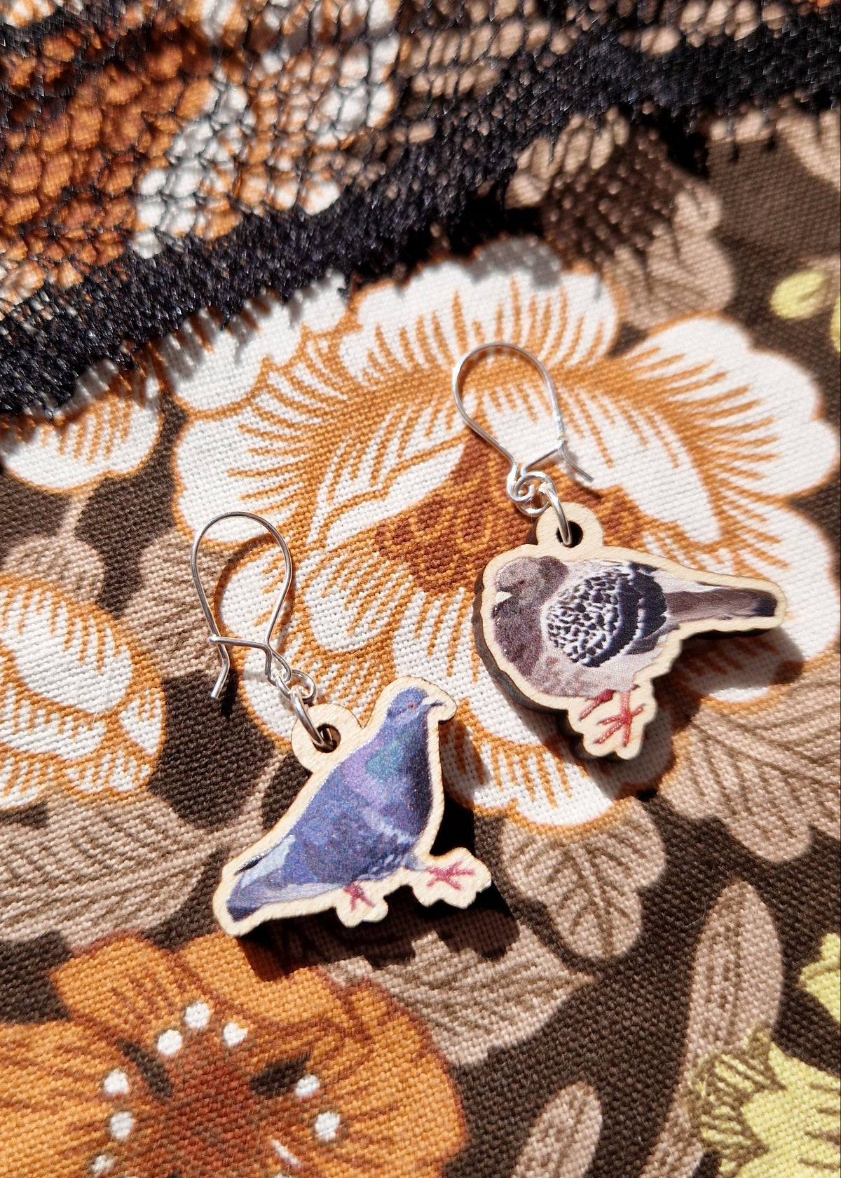 A mismatched pair of pigeon earrings sit on a floral fabric. 