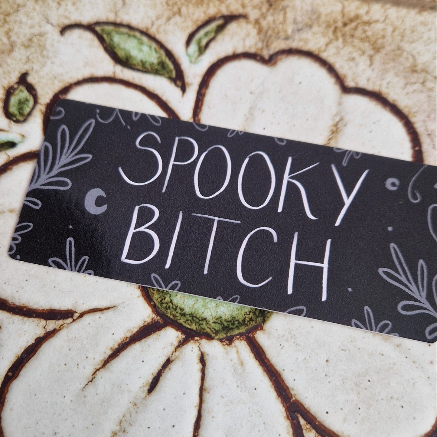 A close up of the spooky bitch sticker showing the illustrations around the edge of the sticker - leafy vines, crescent moons and circles.