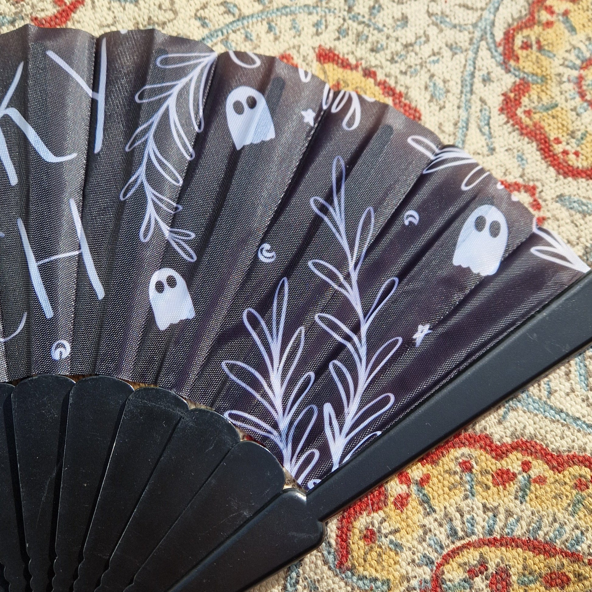 A close up view of the right hand side of the black fan showing the white leafy vines, ghosts, crescent moons and stars. Behind the fan is a patterned rug.