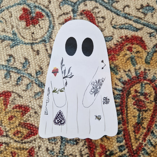 A sticker of a ghost with tattoos sits on a patterned fabric.