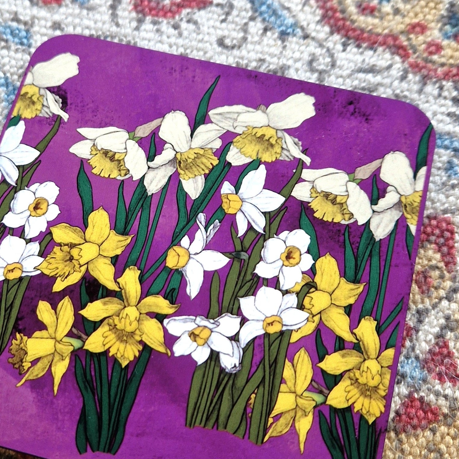 A clop up of the top of the pink square daffodil coaster showing the detail in the bold floral illustration.