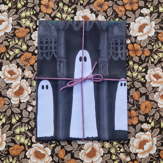 A  folded teatowel sits on a floral patterned background wrapped in a purple twine. Visible on the teatowel are three ghosts floating next to each other surrounded by gothic architecture.