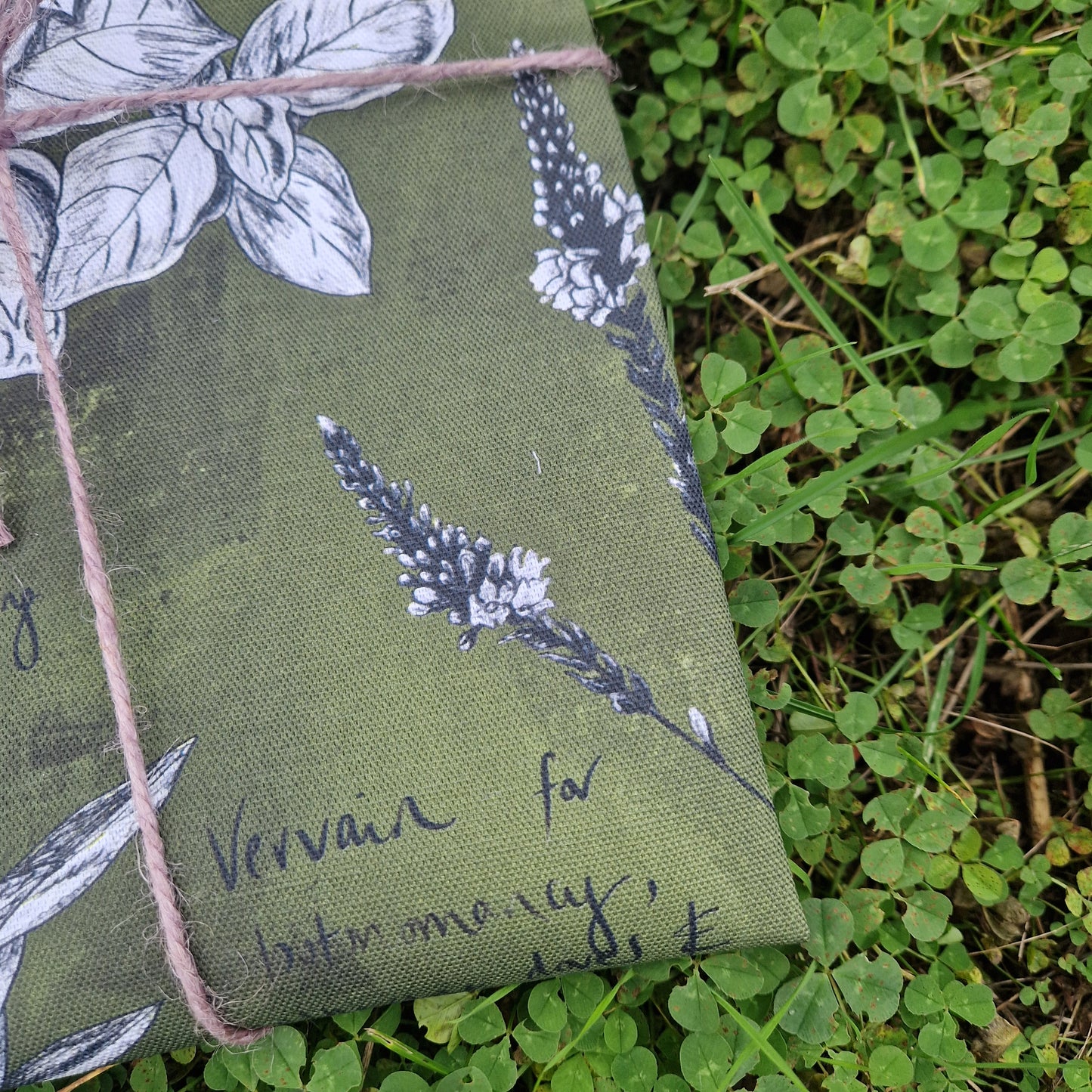 A close up of the bottom right of the green tea towel showing the detail in the white and blackbotanical plant illustrations.