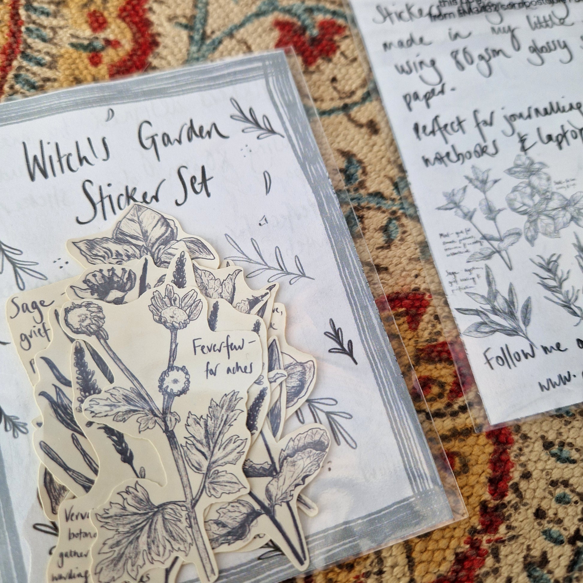 A close up of the front of the witch's garden sticker set showing the plant stickers inside. Behind the sticker set you can see a patterned fabric background and the back of a second witch's garden sticker set.