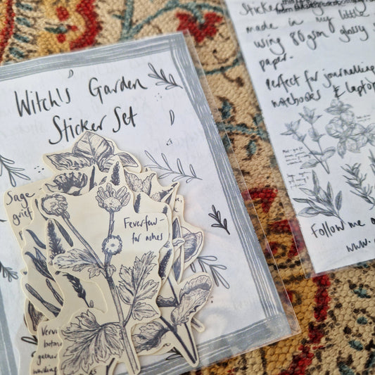 A close up of the front of the witch's garden sticker set showing the plant stickers inside. Behind the sticker set you can see a patterned fabric background and the back of a second witch's garden sticker set.