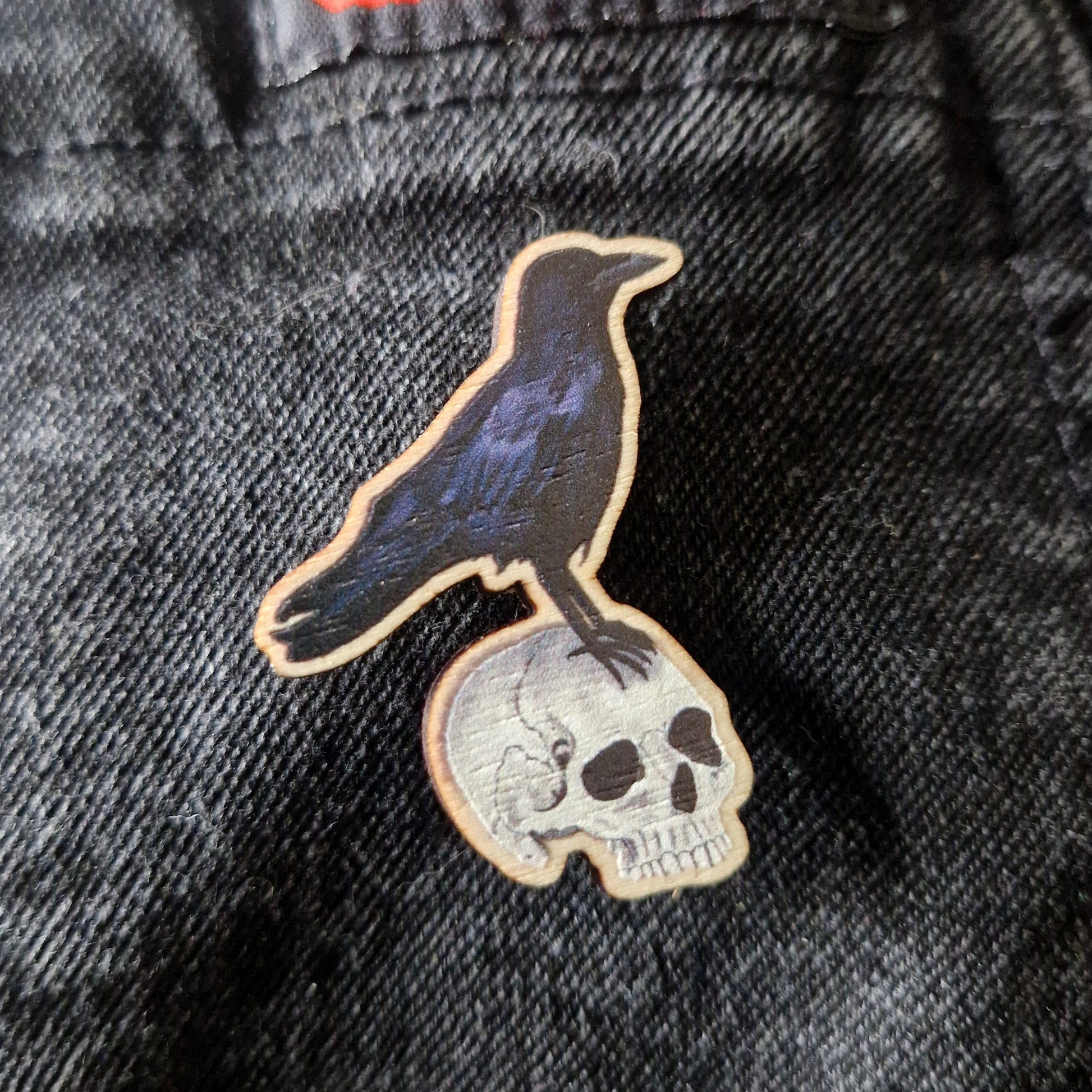Pin with a crow on a skull design on denim dungarees.