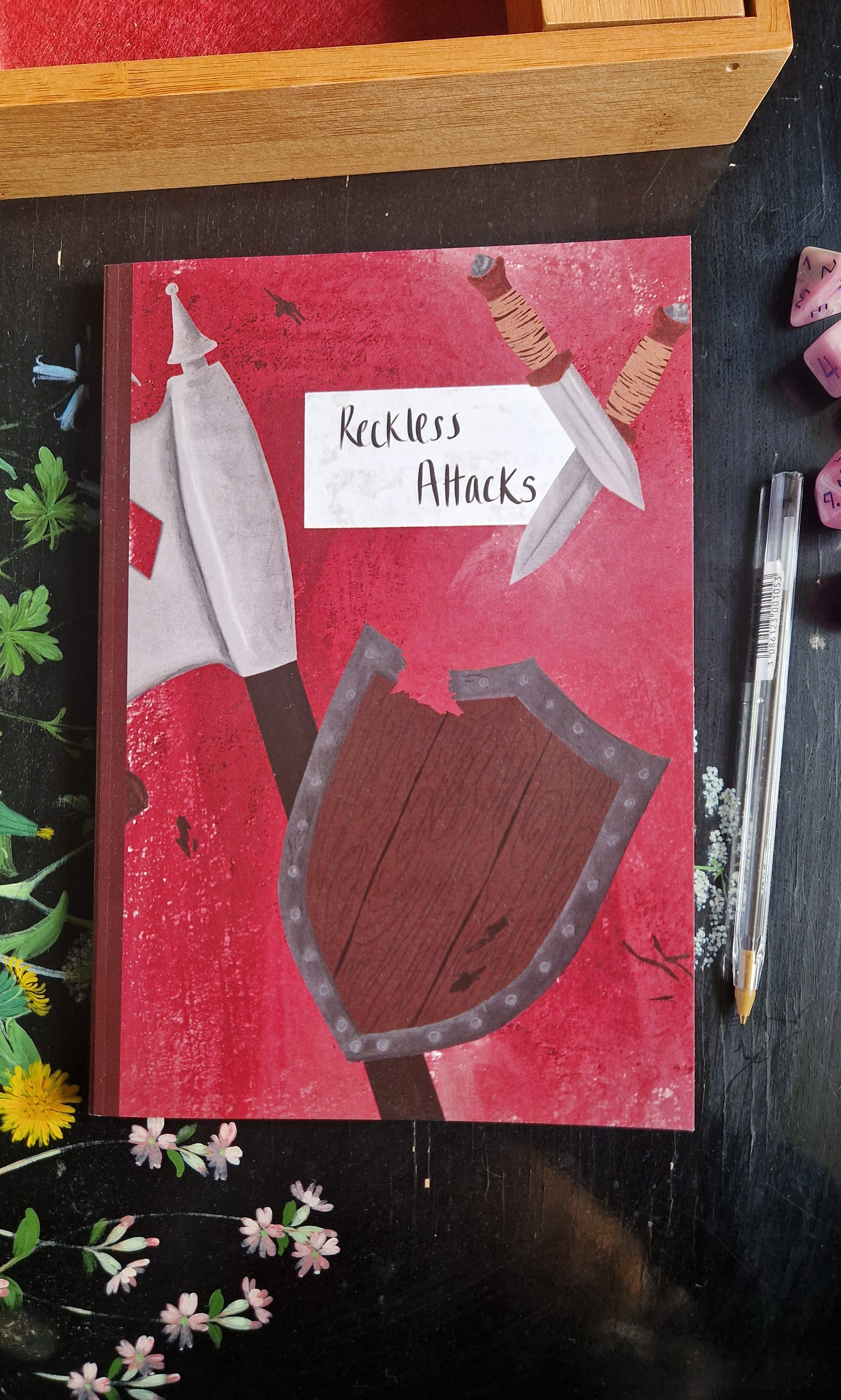 The Reckless Attack Notebook by Duck Egg Designs features a shield and pen on the cover—a perfect barbarian-themed choice for jotting down campaign notes.