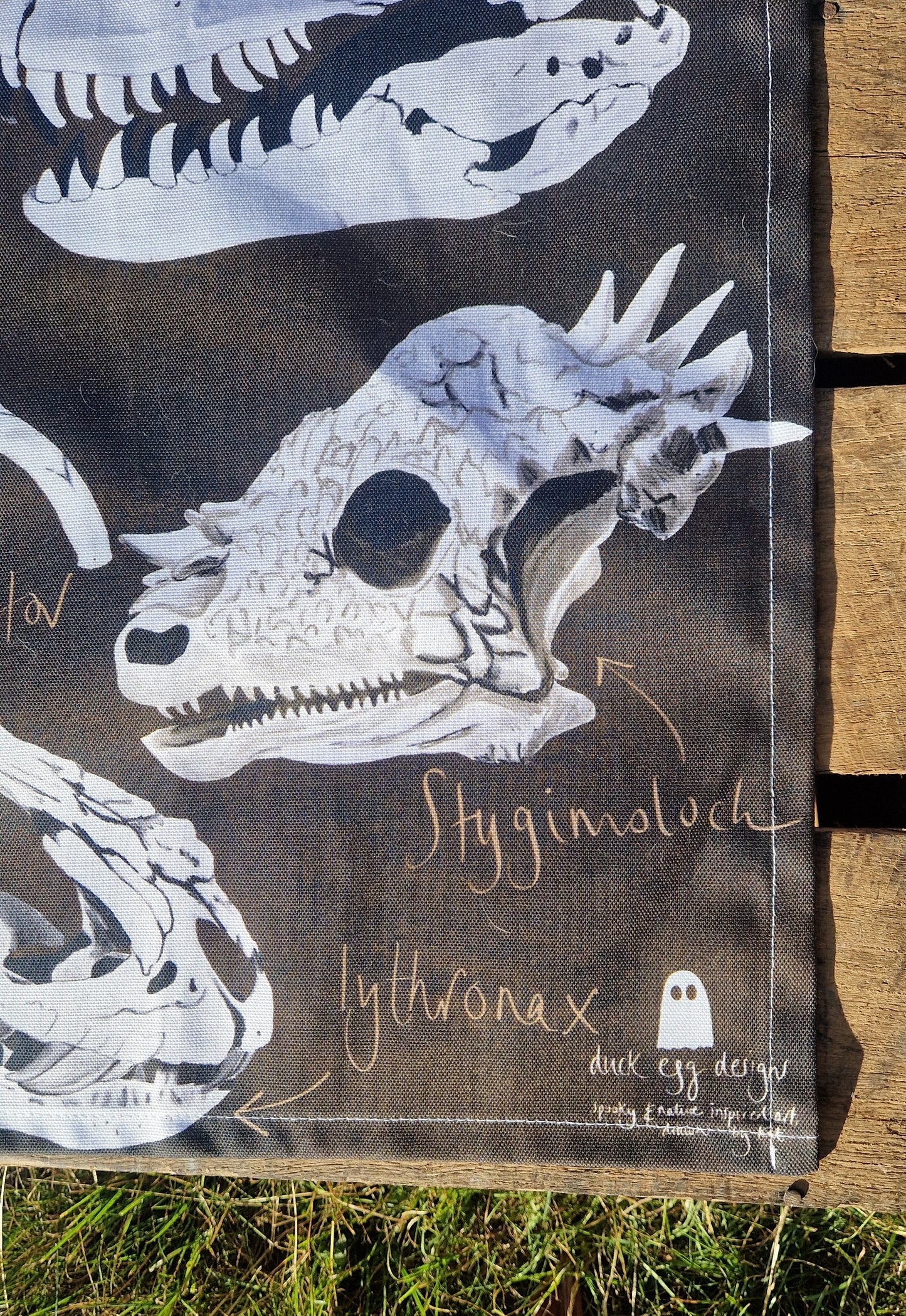 The Dinosaur Tea Towel by Duck Egg Designs is made from 100% cotton and features a detailed Stygimoloch skull illustration with handwritten labels, a small ghost logo, and is proudly made in the UK.
